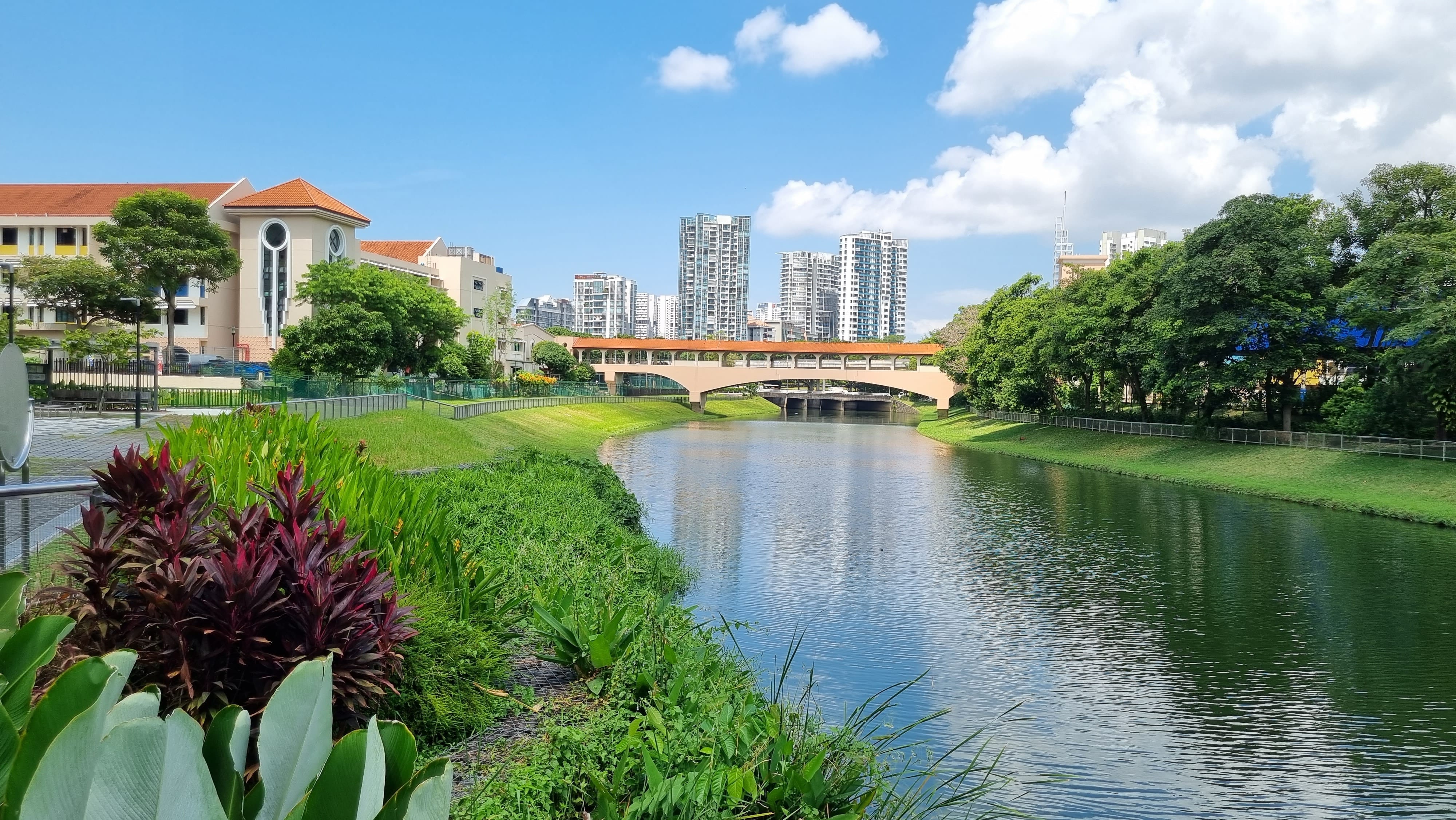 River view in Singapore with buildings and a bridge in the background under a partly cloudy sky.